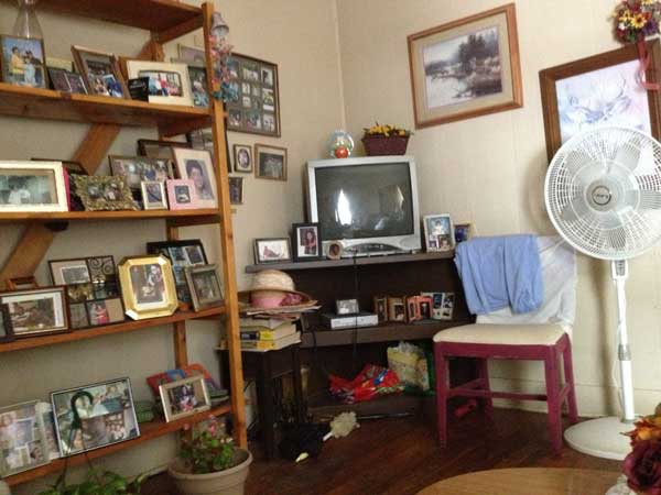 A corner of a living room with a tv, chair, fan, pictures on the wall, and a bookcase filled with framed photos