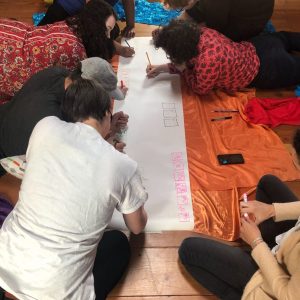 A team gathered around a a long banner of paper, on hands and knees, drawing on the floor.