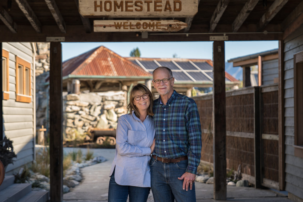 A woman and a man embrace in front of a sheltered pad and a home, with the signs "Homestead" and "Welcome."