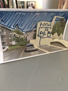 A pop-up sketch of a stand selling pickles, against an image of a city street.