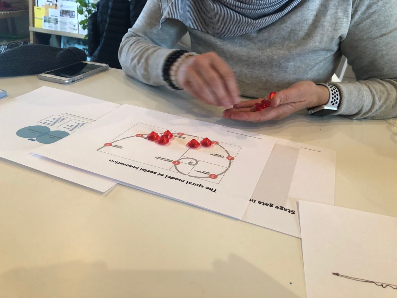 A woman is seen placing plastic jewels on a piece of paper with a spiral and some indecipherable words on it.