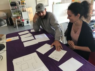 Two team members sit at a table with material stretched in front of them, organizing them.